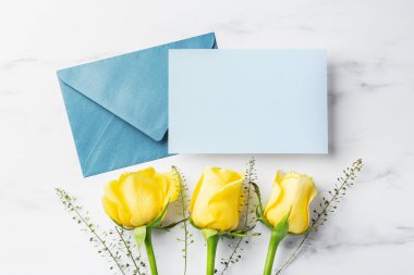 Zarflı mavi kart ve beyaz masa arkasında sarı güller, Babalar Günü hediyesi ve kartı, üst manzara