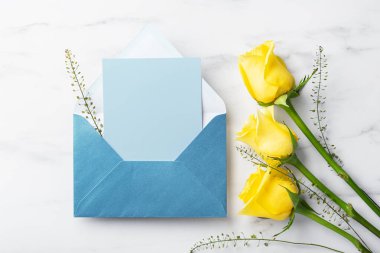 Zarfta mavi kart ve beyaz masa arkasında sarı güller, Babalar Günü hediyesi ve kartı, üst manzara.