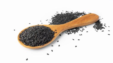 Tahta kaşıkta siyah susam tohumları beyaz arka planda izole edilmiş, yakın plan.