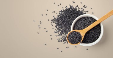 Siyah susam tohumları beyaz kâse üzerinde tahta kaşık kahverengi arka plan, üst görünüm, boşluk kopyala