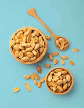 Ahşap kasede yer fıstığı, mavi arka planda kaşık, üst manzara.