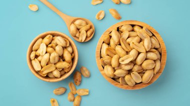 Ahşap kasede kavrulmuş fıstık ve mavi arka planda kaşık.