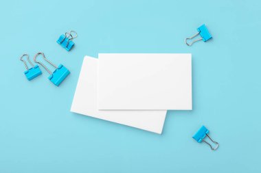 Beyaz kartvizit, mavi arkaplanda ataçlı kağıt modeli, üst görünüm