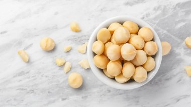 Beyaz kasede Macadamia fındıkları ve mermer mutfak tezgahında çatlak macadamia, yakın plan, üst manzara.