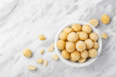 Macadamia fındıkları beyaz kasede, mermer mutfak tezgahında çatlak macadamia, üst manzara, kopyalama alanı.