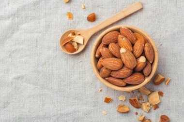 Ahşap kasede kavrulmuş badem ve keten masa örtüsünde kaşık arka plan, üst manzara, boşluk kopyala