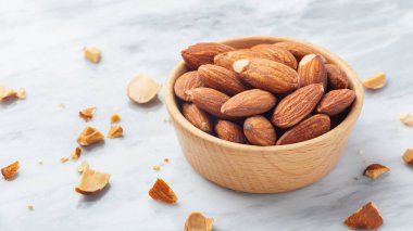 Ahşap kasede badem ezmesi, mermer masa arkasında kırık badem, yakın plan.