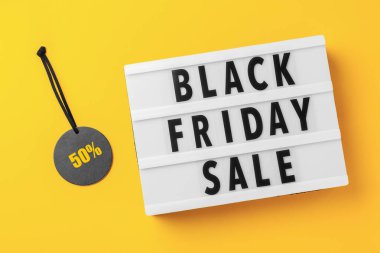 Sarı arka planda satılık etiket olan ışık kutusunda Kara Cuma satışı kelimesi, üst görünüm