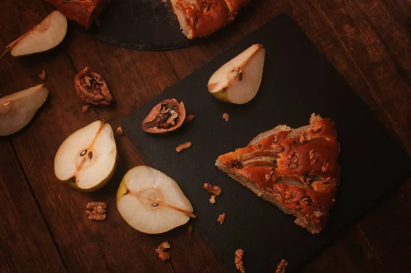 pear pie on a black serving board on a wooden table, cut pears and walnuts lie chaotically