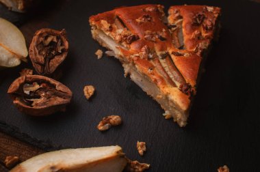 Tahta bir masada, siyah bir servis tahtasında armut dilimi ve ceviz kaotik bir şekilde yatar.