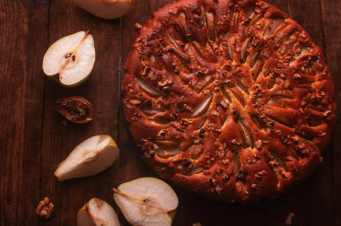 Tahta bir masada, siyah bir servis tahtasında armut dilimi ve ceviz kaotik bir şekilde yatar.
