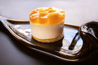 Koyu arkaplanda şarap şişesinden yapılmış bir tabakta mangolu turtalı sufle keki.