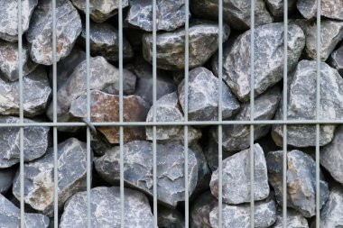 Çiğ kayaların sınırı ve gri taşların duvarı, doğal taşların arka planında, metal ızgaralarda ezilmiş ve pürüzlü maddeler, gri renkte devasa sınırlar, bahçeler için doğal mineral arka planıdır.