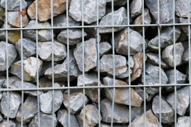 Çiğ kayaların sınırı ve gri taşların duvarı, doğal taşların arka planında, metal ızgaralarda ezilmiş ve pürüzlü maddeler, gri renkte devasa sınırlar, bahçeler için doğal mineral arka planıdır.