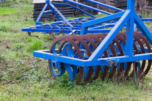 Blue heavy agricultural equipment like plow with sharp steel discs for agricultural field cultivation with tractor-drawn equipment for field work preparation facilitates hard farm work mechanization