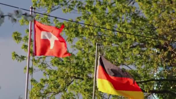 在多风的日子里 瑞士国旗和德国国旗肩并肩地展示着瑞士 德国的友谊和德国与飘扬的国旗的关系 以此作为政府合作和冲突或协议的象征 — 图库视频影像
