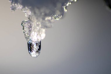 Eriyen buzdan dökülen kristal berrak su damlasıyla eriyen buz sarkıtı küresel ısınma etkisini ve eriyen buzullar için iklim değişikliğini gösteren buz saçakları, parlak güneş gününde kışın sona erdiğini gösteriyor.