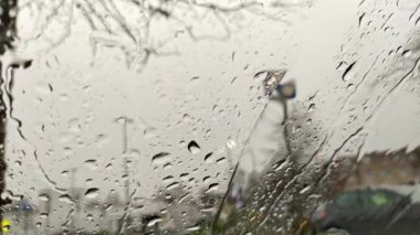 Şehir sokaklarının bulanık arka planına sahip araba camındaki yağmur damlaları kışın yağmurlu bir günde sağanak ve damlayan yağmur damlaları gök gürültülü fırtınalarda ve araba camlarında şiddetli yağış