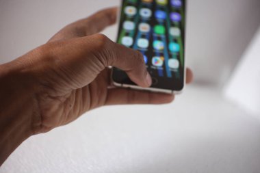 Bir adamın eli, beyazda izole edilmiş siyah bir akıllı telefonu tutuyor.