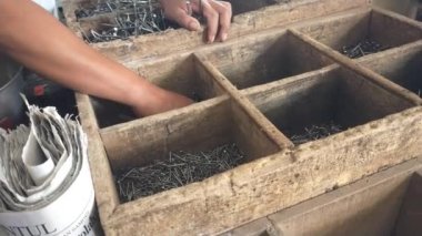 Bir inşaat malzemesi satıcısı elle tartmak için çivi topluyor..