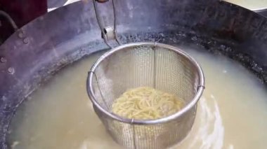 Erişteyi büyük bir kızartma tavasında pişirme işlemi. Erişte makinesi, sokak yemeği.