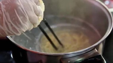 Yemek çubuklarıyla erişte pişirip bir kaseye, sokak yemeklerine koyuyorlar.