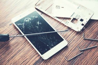 Ahşap masadaki aletlerle kırılmış akıllı telefon.