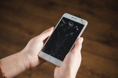 Kadın eli kırık, kahverengi arka planda akıllı telefon.