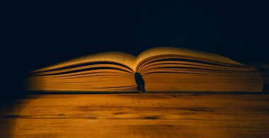 Koyu arkaplanda tahta masanın üzerinde açık bir kitap var.