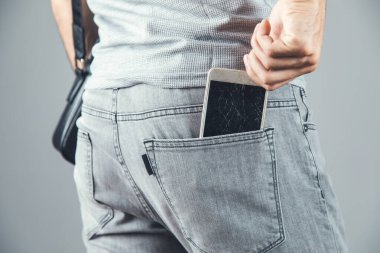 Gri arka planda adamın eli kırık cep telefonu.