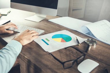 Ofiste çalışan bir iş adamı. Masasında bilgisayar ve grafik dokümanları var..