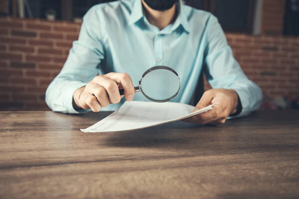 Businessman readng documents with magnifying glass in office