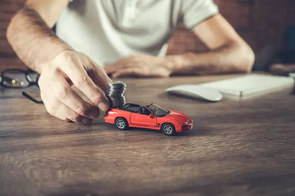 man hand holding model of  car and coins