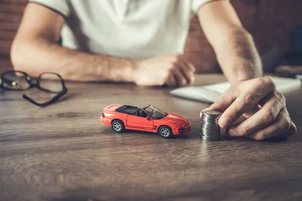 man hand holding model of  car and coins