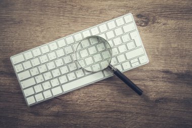 Tahta arka plandaki beyaz klavyede büyüteç