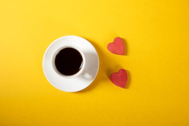 Sarı zemin üzerinde bir fincan kahve olan ahşap kırmızı kalpler.