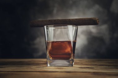 Ahşap arka planda bir bardak viski ve puro.