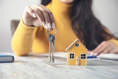 Çalışma masasında anahtarı olan ev modelini tutuyor.