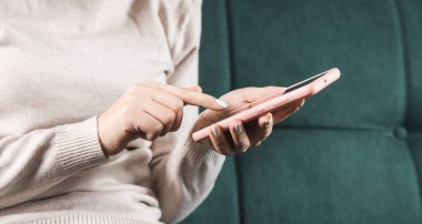 Kanepede oturan akıllı telefonu kullanan genç bir kadın.