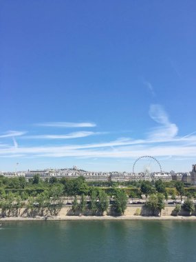 Paris 'teki Seine Nehri manzarası, bereketli ağaçlar, klasik mimari ve dönme dolap. Montmartre ve Sacre-Coeur açık mavi gökyüzünün altında. Simgesel şehir manzarası.