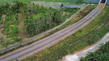 Yeşil ağaçlar ve dağlar arasındaki karayolu ve demiryolu raylarının hava aracı görüntüsü