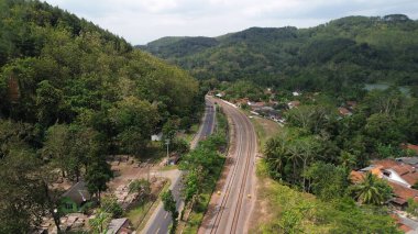 Yeşil ağaçlar ve dağlar arasındaki karayolu ve demiryolu raylarının hava aracı görüntüsü