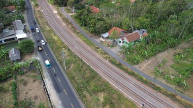 Yeşil ağaçlar ve dağlar arasındaki karayolu ve demiryolu raylarının hava aracı görüntüsü