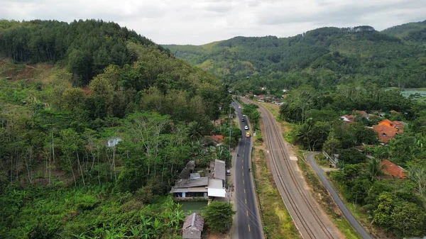 Yeşil ağaçlar ve dağlar arasındaki karayolu ve demiryolu raylarının hava aracı görüntüsü