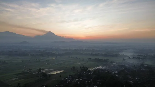 インドネシアの田畑と木の朝霧で背景にあるメリピ山とメリバブ山との霧の日の出 — ストック写真