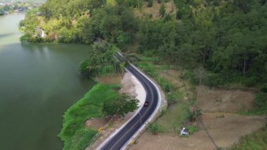 Endonezya 'daki Serayu nehri ile yeşil ormanlar arasındaki yolun insansız hava aracı görüntüsü
