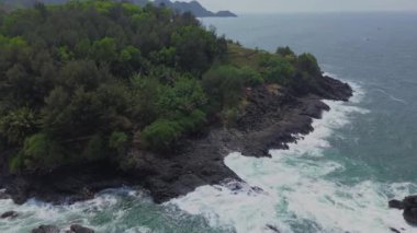 İnsansız hava aracı manzarası Menganti Sahili, Kebumen, Central Java, Endonezya, sakin deniz dalgaları, mercan kayalıkları ve yeşil ağaçlarla dolu bir sahil.