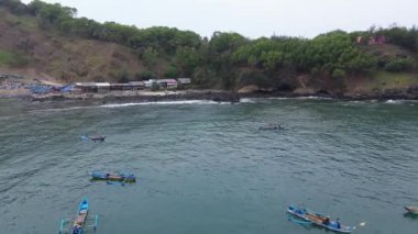 Menganti Beach Kebumen Central Java Endonezya 'nın insansız hava aracı görüntüsü, beyaz kumlu plaj, sakin dalgalar, uçurumlar ve yeşil ağaçlar ve geleneksel balıkçıların ve geleneksel balıkçı teknelerinin faaliyetleri
