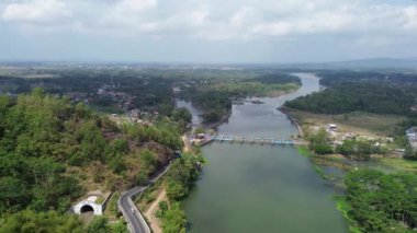 Endonezya 'daki Serayu nehri ile yeşil ormanlar arasındaki yolun insansız hava aracı görüntüsü