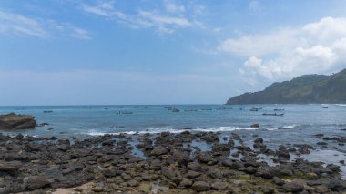 Menganti Beach Kebumen Central Java Endonezya plajının beyaz kum, sakin dalgalar, uçurumlar ve yeşil ağaçlarla insansız hava aracı görüntüsü ve geleneksel balıkçıların ve geleneksel balıkçı teknelerinin faaliyetleri